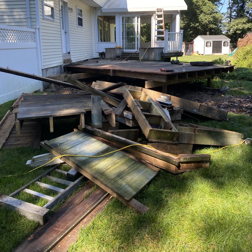 Deck torn apart and piled on the lawn behind a house, ready for demolition debris removal
