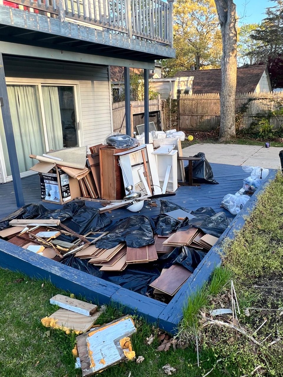 Pile of old furniture, wood, and trash bags on a backyard deck ready for junk removal